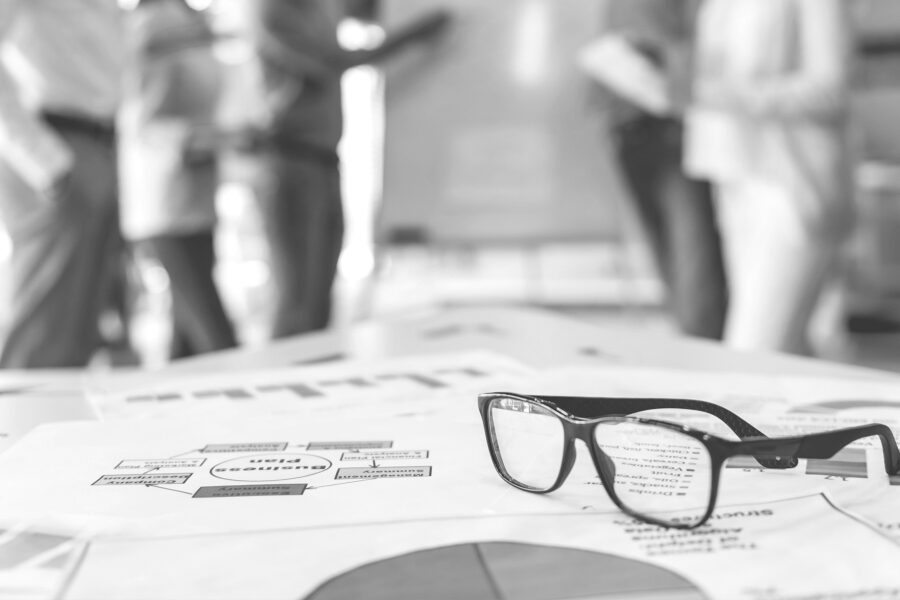 A group of co-workers are collaborating in the background blurred with a pair of glasses in focus.